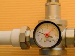 Un réducteur de pression d'eau avec un manomètre indiquant 1 bar. L'appareil est monté sur un tuyau blanc.