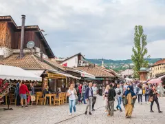 Tłum ludzi spaceruje po tętniącym życiem rynku w Sarajewie, gdzie można kupić pamiątki i zjeść. Widać, że czy Sarajewo jest bezpieczne, bo wszyscy czują się swobodnie.