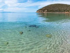 Piękne livorno plaże z krystalicznie czystą wodą i piaszczystym dnem. W oddali widać żaglówkę i zielone wzgórza.