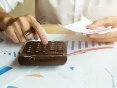 Ręce liczą rachunki na kalkulatorze, analizując wykresy. Wzrost cen energii wpływa na budżet.