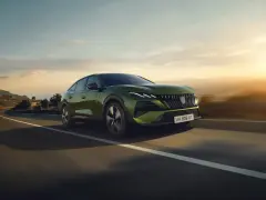Zielony Peugeot 408 GT sunie po krętej drodze, otoczony malowniczym krajobrazem o zachodzie słońca.