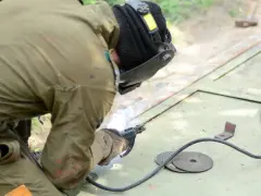 Spawacz w masce i rękawicach używa elektrod spawalniczych do łączenia metalu. Iskry sypią się podczas pracy.