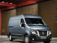 Szary Nissan NV400 stoi przed brązową, perforowaną ścianą w industrialnym wnętrzu.
