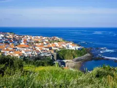 Malownicze miasteczko na wybrzeżu Portugalii, z białymi domami i pomarańczowymi dachami, nad błękitnym oceanem. Ceny wakacji w Portugalii mogą być zaskakująco przystępne.