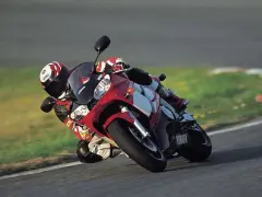 Motocyklista na torze pochyla się na swoim czerwono-białym motocyklu Yamaha R6 2001, w pełni ubrany w kombinezon i kask.