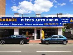 Garage avec enseigne bleue et jaune, deux voitures garées devant, sous un ciel bleu avec des nuages.