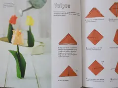 Vackra vika pappersblommor i form av tulpaner, en klassiker inom origamikonsten. En orange tulpan i förgrunden, med en röd och en gul i bakgrunden.