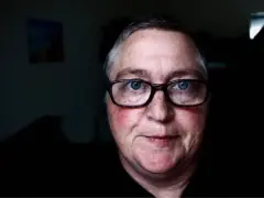 Mężczyzna z niebieskimi oczami i okularami. Jego **czerwona twarz** emanuje ciepłem, a na policzkach widać rumieńce.
