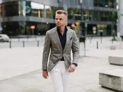 Elegancki mężczyzna w szarej marynarce w kratę i białych spodniach. Idealne połączenie, jeśli zastanawiasz się, jakie spodnie do szarej marynarki pasują.
