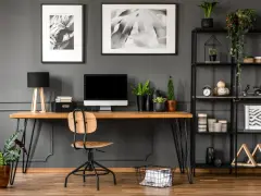 Arredamento studio casa: scrivania in legno con computer, sedia, piante e libreria nera piena di oggetti decorativi.