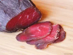 Bresaola co to? Ciemnoczerwone, cienko pokrojone plastry suszonej wołowiny na desce.