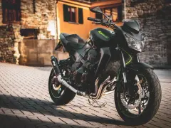 Czarny motocykl Kawasaki na brukowanej ulicy, z budynkami w tle.