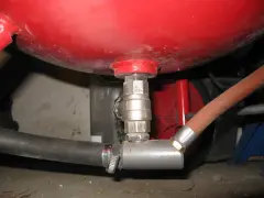 Metalowy zawór talerzowy do piaskarki, podłączony do czerwonego zbiornika i węży.