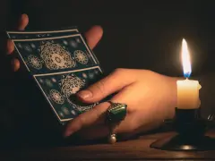 Dłoń trzyma karty tarota przy blasku świecy. Czy to karta Cesarz?