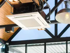Unidad de cassette de un sistema VRV integrada en un techo de madera y metal, con luces y tuberías visibles.