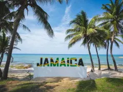 Napis "JAMAICA" na tle plaży, morza i palm.