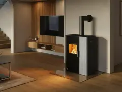 Estufa mixta pellets y leña canalizable, con fuego encendido, en un salón moderno con escaleras y TV.