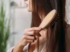 Eine Frau kämmt ihr langes, dunkles Haar mit einer Holzbürste. Sie achtet auf ihre Haare, um Haarausfall bei Frauen im Alter vorzubeugen.