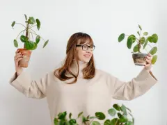 Mujer sonriente con gafas sostiene dos plantas altas de interior.