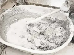 Mieszanie wapna palonego z wodą w dużej misie, tworząc gęstą, szarą masę.
