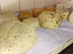 Różne rodzaje serów owczych, niektóre z ziołami, inne z papryczką, prezentowane na białym obrusie.