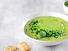 Cremoso hummus di piselli guarnito con piselli freschi, basilico e semi di sesamo, servito con cracker croccanti.