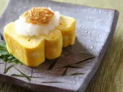 Delikatny omlet tamago, zwinięty w rolki, podany z tartą rzodkwią i grzybami enoki na talerzu z bambusowym wzorem.