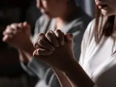 Two women pray, hands clasped. One's face is blurred, the other's lips are visible. This scene evokes the devotion of a deaconess in the bible.