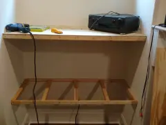DIY project: a drill, screws, and audio receiver are on a shelf, with a wooden frame below, ready for how to hang shelves.