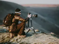 Man med ryggsäck och kamera på stativ, redo att omskola sig till naturfotograf i gryningen.