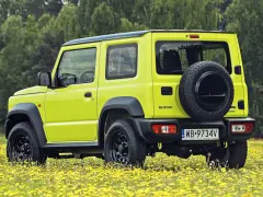 Jaskrawożółty Suzuki Jimny na tle łąki z żółtymi kwiatami. Sprawdź aktualną suzuki jimny cena i wybierz się na przygodę!