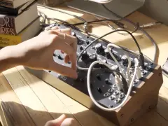 Ręka manipuluje pokrętłami na syntezatorze Moog DFAM, tworząc dźwięki.
