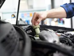Ręka mechanika dokręca korek zbiorniczka płynu hamulcowego. Czas na badanie techniczne po terminie, by uniknąć problemów.