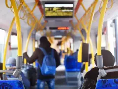 Wnętrze autobusu z żółtymi poręczami. Młody mężczyzna z niebieskim plecakiem idzie do tyłu. Uważaj, by nie dostać mandatu za brak biletu.