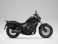 Czarny motocykl Honda Rebel 500 z sakwami, gotowy na podróż. Jego prędkość maksymalna pozwala na swobodne pokonywanie tras.