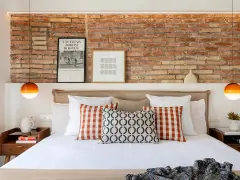 Ideas para decorar la pared de la cabecera de la cama: ladrillo visto, cuadros y lámparas naranjas.