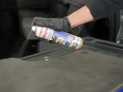 Mano con guanto nero spruzza spray Idrostop su tessuto grigio per impermeabilizzare.