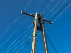 Słup energetyczny z przewodami na tle błękitnego nieba. Zastanawiasz się, ile wynosi odszkodowanie za słupy energetyczne na działce?