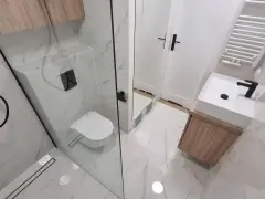 Nowoczesna łazienka z prysznicem walk-in, umywalką nablatową i podwieszaną toaletą. Eleganckie płytki imitujące marmur i drewniane akcenty. Remont łazienki koszt może być różny, ale efekt jest wart inwestycji.