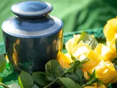 Niebieska urna pogrzebowa obok bukietu żółtych róż, kwiatów symbolizujących śmierć i pożegnanie.