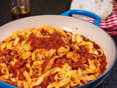 Herzhafte Tagliatelle mit einer reichhaltigen alla bolognese Sauce in einer blauen Pfanne, bereit zum Servieren.