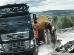Ciężarówka Volvo FH16 750 z naczepą przewozi żółty wozidło przegubowe przez kamieniołom.