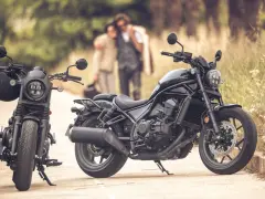 Dos motos negras, una con casco, listas para un viaje. Una pareja abraza en el fondo, disfrutando del paisaje. Una moto sin marchas, perfecta para la aventura.