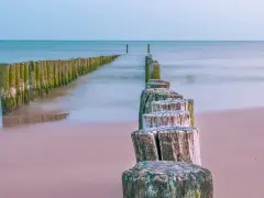 Drewniane pale tworzą ścieżkę wzdłuż plaży, prowadzącą w stronę morza. To idealne miejsce na spacer, odkrywając kąty rybackie trasę.