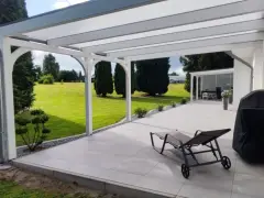 Moderne Terrasse bauen: Überdachter Sitzbereich mit Liegestuhl, Grill und Blick ins Grüne.