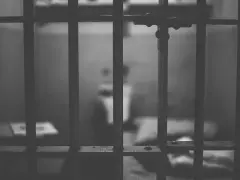 Widok przez kraty więzienne. W tle niewyraźna postać, symbolizująca nadzieję na wcześniejsze zatarcie skazania i nowe życie.