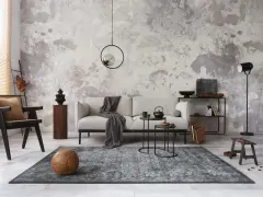 Salon w stylu minimalistycznym z szarą sofą, czarnym fotelem i dywanem. Na ścianie betonowa faktura.