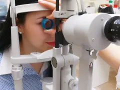 Kobieta podczas badania dna oka przy użyciu specjalistycznego sprzętu. Okulista dokładnie sprawdza wzrok pacjentki.