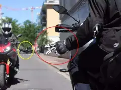 Mano guantata che fa il segno di pace, un gesto del linguaggio motociclisti. Un'altra moto in lontananza.