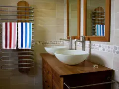 Salle de bain moderne avec double vasque. L'arrivée d'eau est discrète, deux lavabos blancs reposent sur un meuble en bois. Deux serviettes rayées sèchent sur un radiateur.